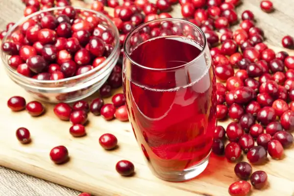 Un verre de jus de cranberry rouge vif, entouré de baies fraîches. Est-ce que le cranberry fait uriner ? Cette boisson est connue pour ses bienfaits.