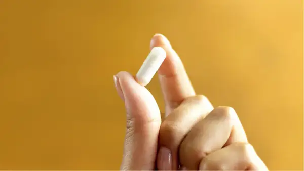 Main tenue pour votre bien-être : 1g de vitamine C par jour, une capsule blanche tenue entre le pouce et l'index.