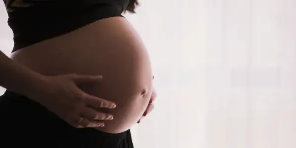 Gros plan sur le ventre arrondi d'une femme enceinte, ses mains le caressant. Un signe que la perte du bouchon muqueux approche.