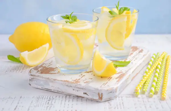 Deux verres de limonade pétillante avec des tranches de citron et des feuilles de menthe. Un citron entier et une tranche sont à côté. Parfait pour soulager les gaz intestinaux.