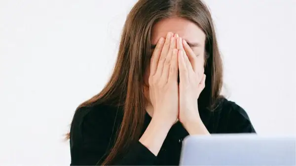 Une jeune femme, le visage caché par ses mains, exprime une **énorme fatigue** devant son ordinateur.